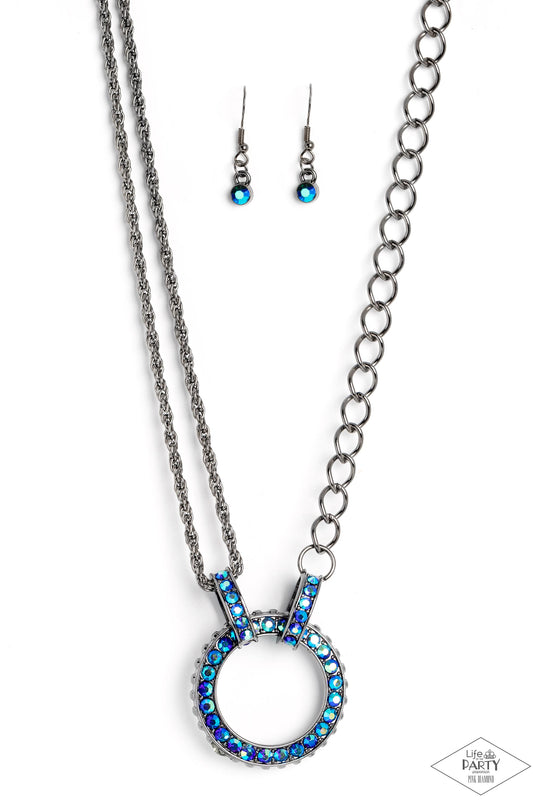 Paparazzi Accessories Razzle Dazzle - Blue A collision of mismatched gunmetal chains gives way to a studded gunmetal pendant that has been encrusted in glittery blue UV rhinestones. The result is a gritty, industrial design with endless attitude. Features