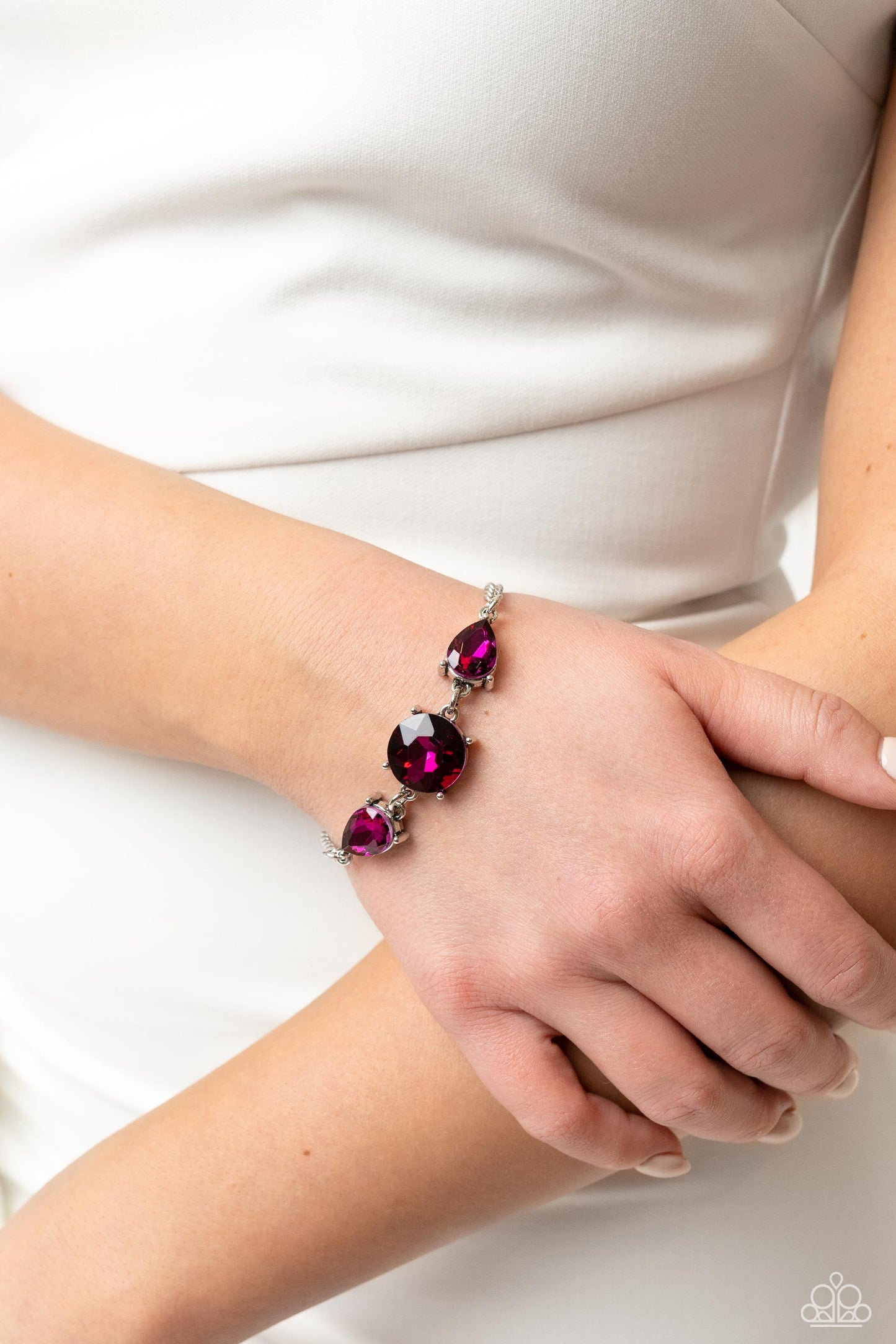 Paparazzi Accessories Twinkling Trio - Pink An oversized round gem bordered by teardrop gems cluster together to create a glittery silver collection around the wrist. Featured in a fuchsia hue, each gem reflects light off of its faceted surface emitting f
