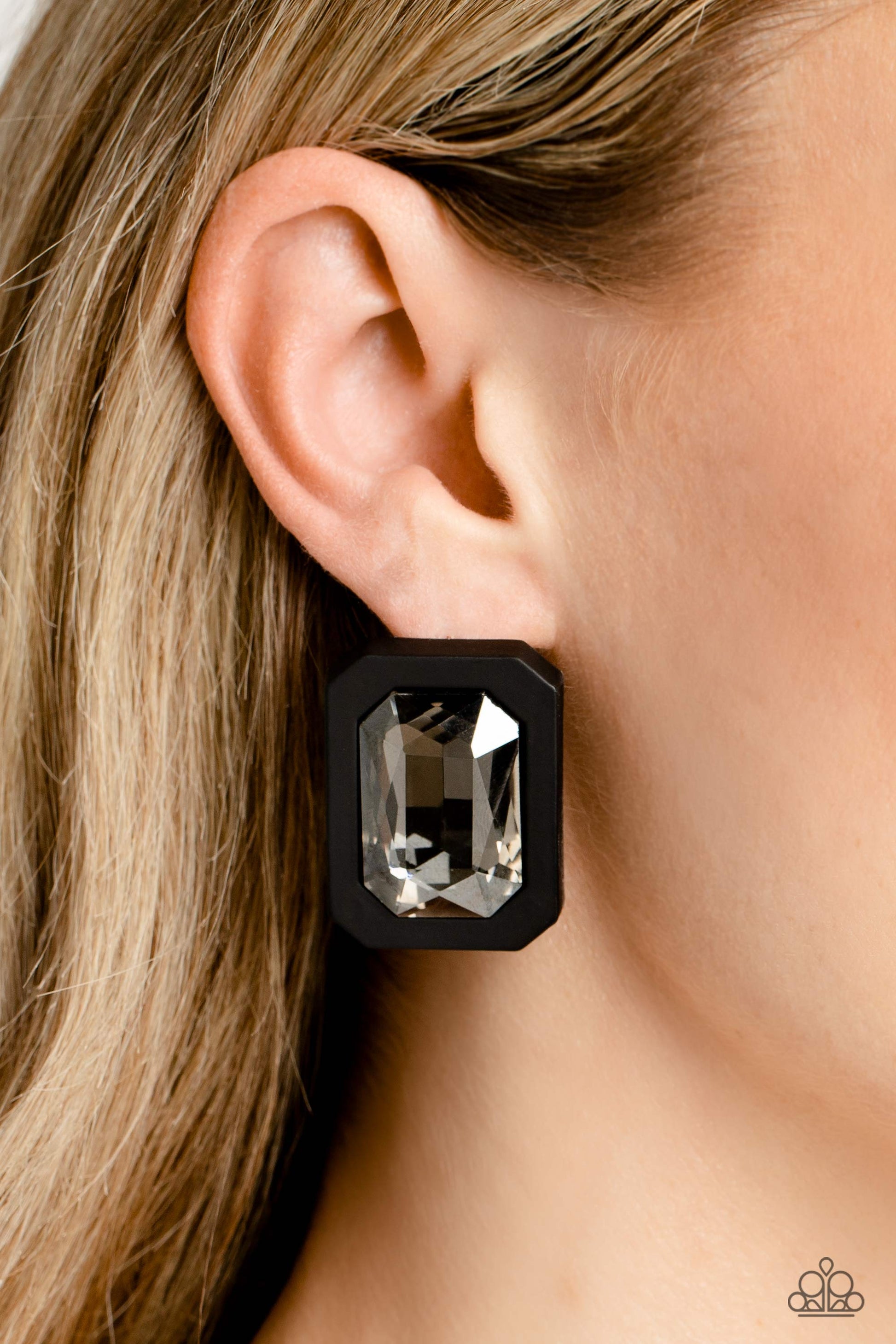 Paparazzi Accessories Edgy Emeralds - Black Standing out against a black rubber backdrop, an oversized, faceted emerald-cut gem shimmers and shines for an edgy sparkle against the ear. Earring attaches to a standard post fitting. Sold as one pair of post