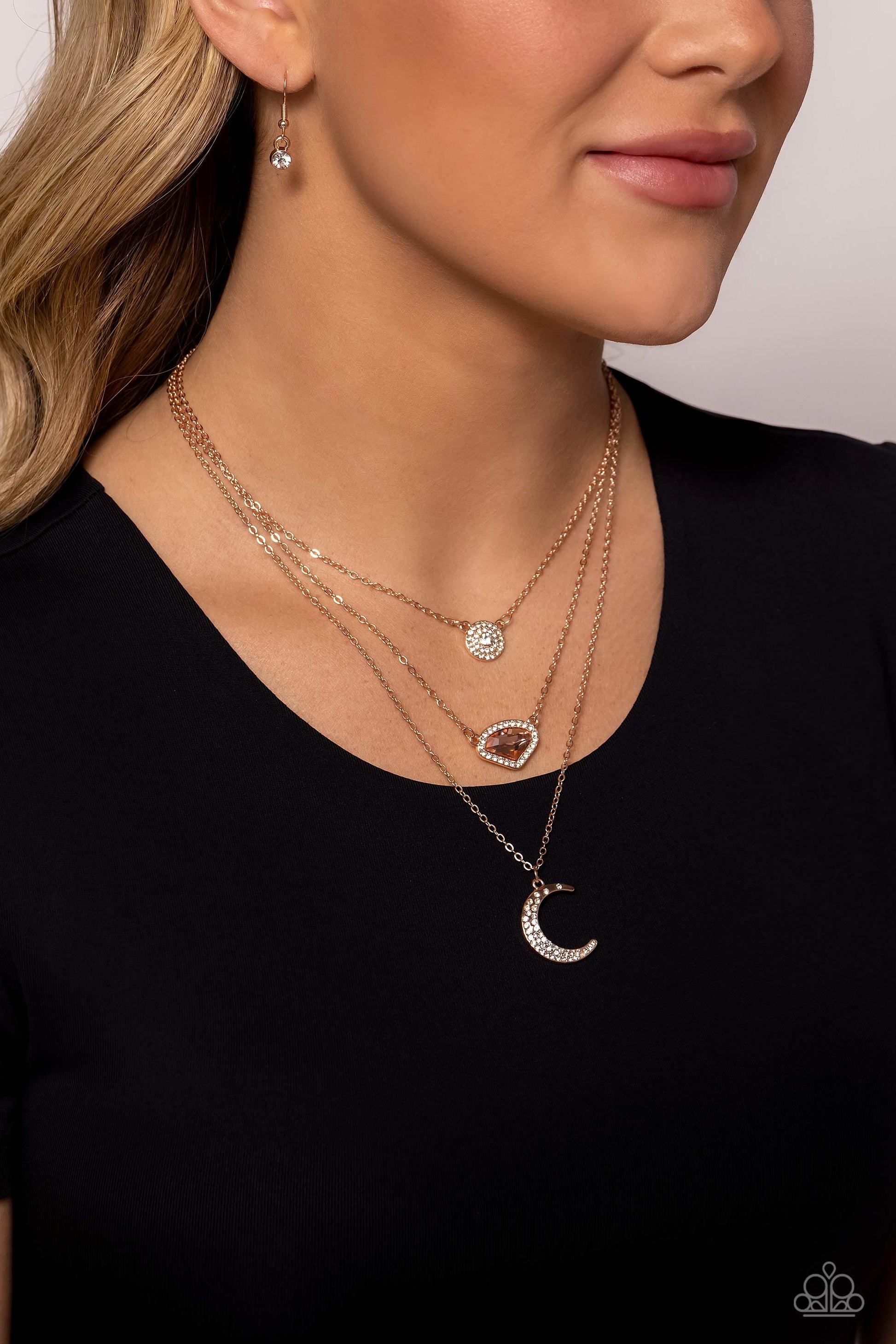 Paparazzi Accessories Lunar Lineup - Rose Gold Three shimmery rose gold chains, infused with three stellar pendants, layer across the chest in a celestial display. A dainty, white rhinestone-encrusted, rose gold pendant with a white center swings from the
