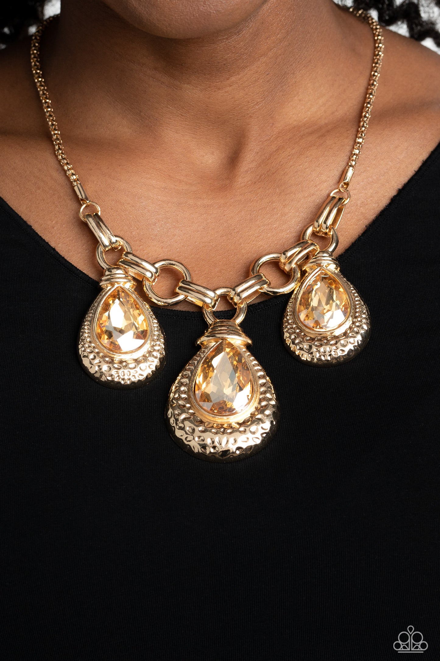 Paparazzi Accessories Built Beacon - Gold Oversized links of gold are artfully interlocked, laying the groundwork for a dynamic display of industrial grit. A trio of oversized champagne, faceted, teardrop gems drips from the chainlinks above, each set ins
