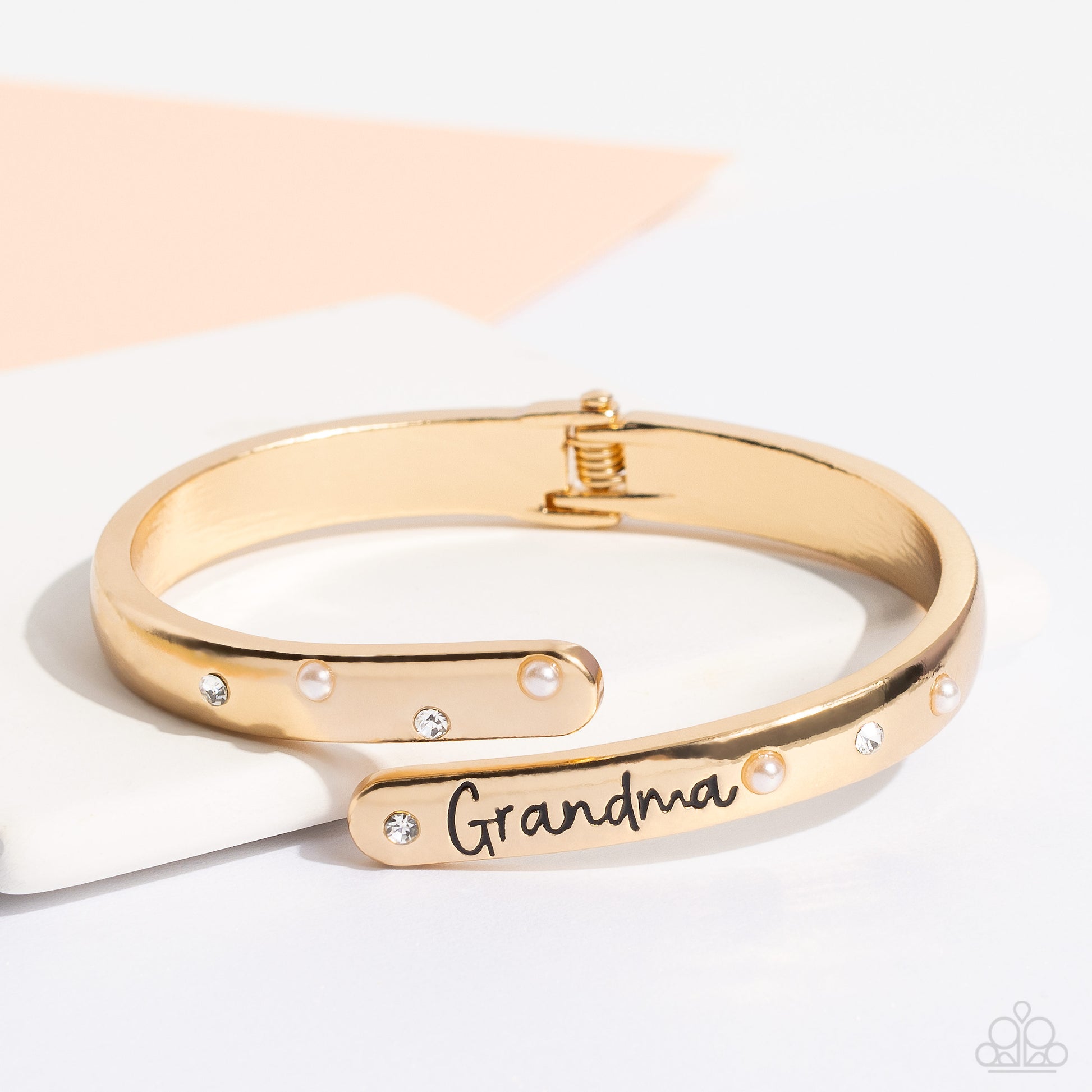 Paparazzi Accessories Gorgeous Grandma - Gold High-sheen gold curves into a hinged closure around the wrist. Featured on the upper curve, dainty pearls and white rhinestones alternate in a zig-zag pattern for a refined shimmer. The lower curve of gold fea