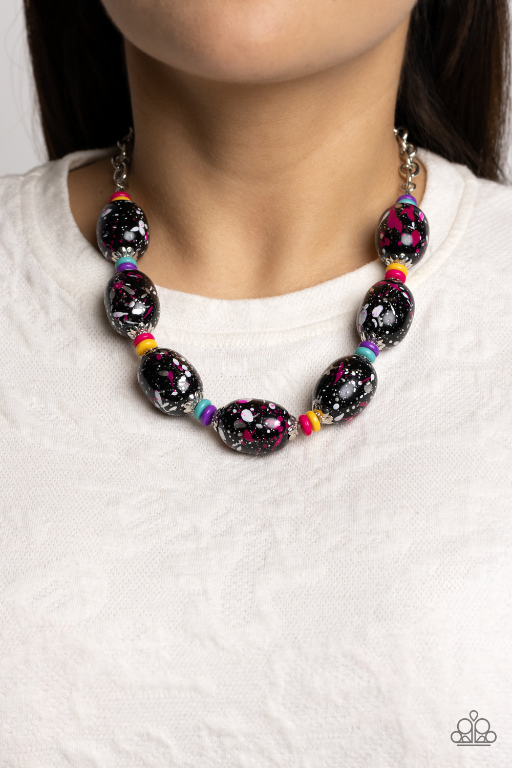 Paparazzi Accessories No Laughing SPLATTER - Pink Featuring a hot pink, white, and silver paint splatter, oversized black beads loop around the collar from a classic silver link chain. Silver floral fittings and small discs in shades of hot pink, yellow,