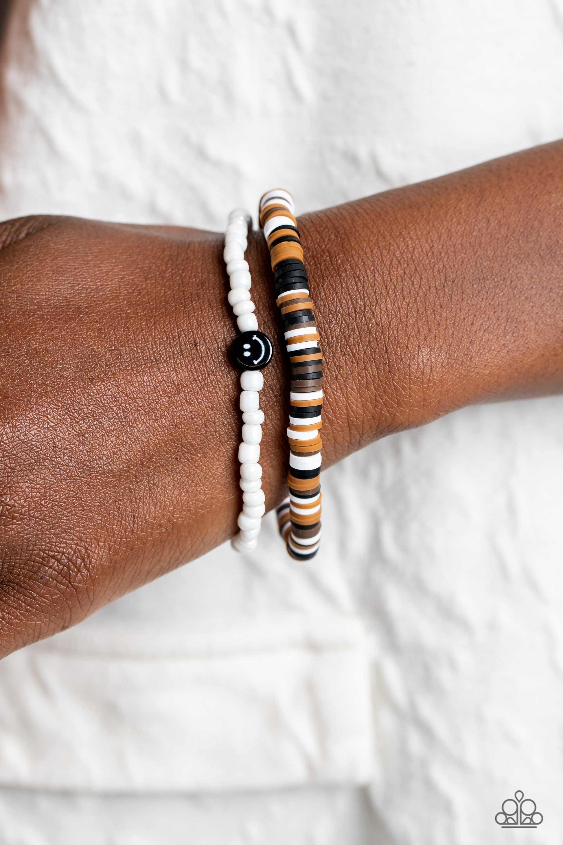 Paparazzi Accessories Tabloid Talent - Black Black, tan, white, and brown clay discs combine with a strand of white seed beads to provide a vibrant pop of color along the wrist. Sporadically dotted in the high-sheen seed bead strand, black smiley face bea