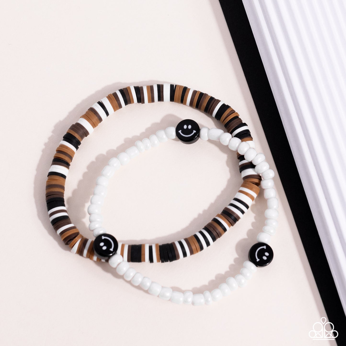 Paparazzi Accessories Tabloid Talent - Black Black, tan, white, and brown clay discs combine with a strand of white seed beads to provide a vibrant pop of color along the wrist. Sporadically dotted in the high-sheen seed bead strand, black smiley face bea