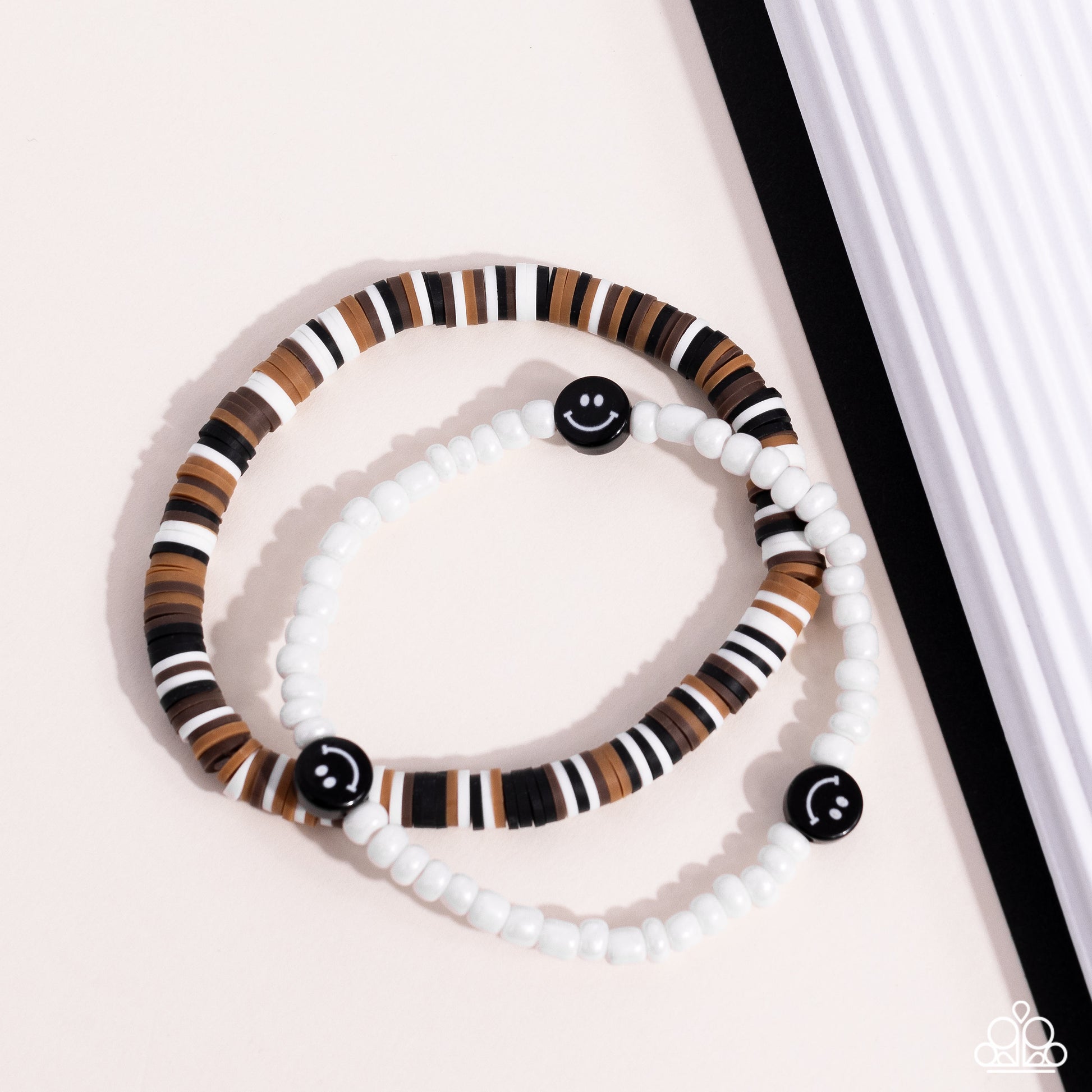 Paparazzi Accessories Tabloid Talent - Black Black, tan, white, and brown clay discs combine with a strand of white seed beads to provide a vibrant pop of color along the wrist. Sporadically dotted in the high-sheen seed bead strand, black smiley face bea