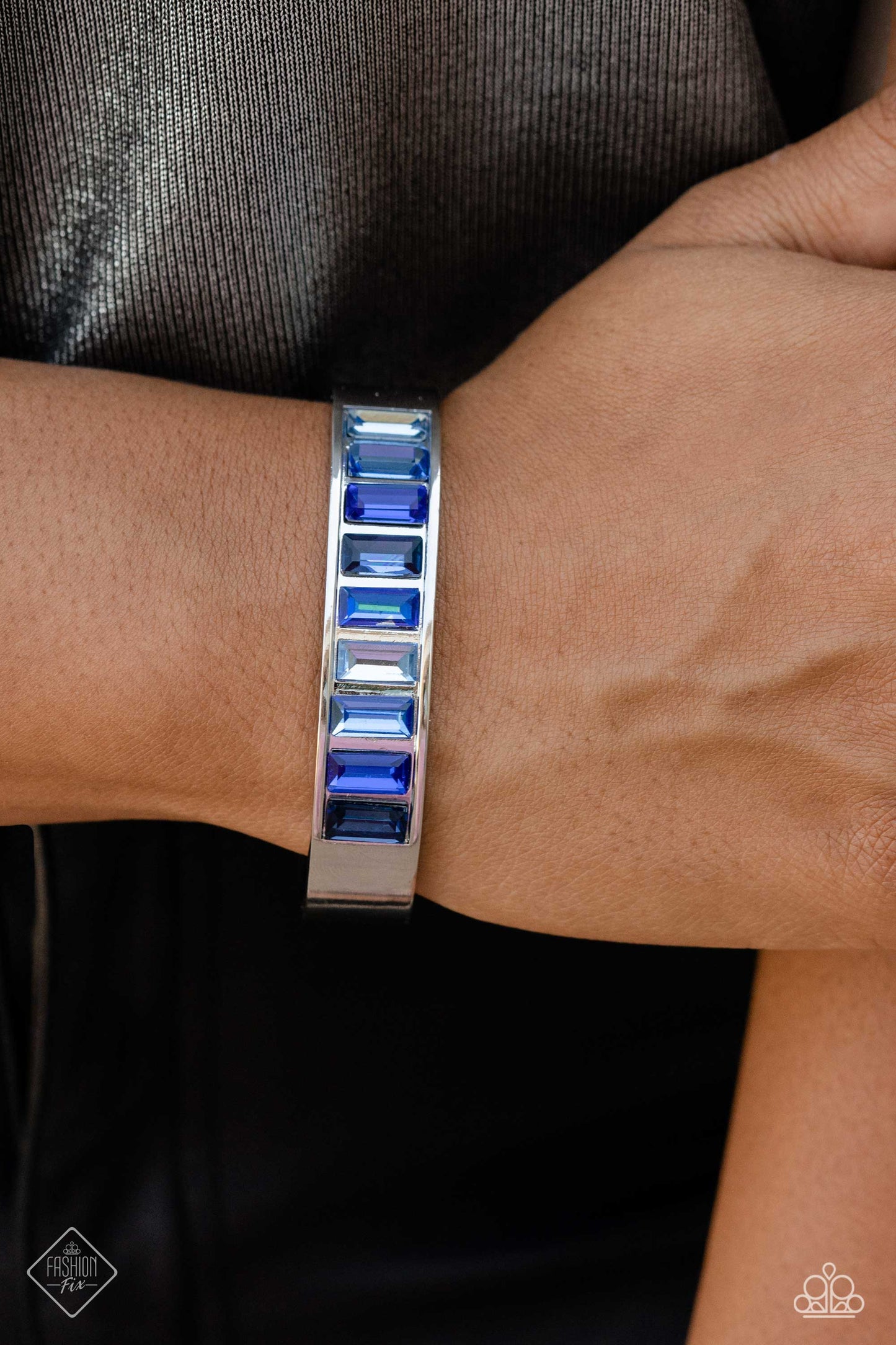 Paparazzi Accessories Practiced Poise - Blue Embedded in the center of a thick, high-sheen silver cuff, a row of glassy emerald-cut gems in varying shades of blue radiates atop the wrist, creating an unexpected pop of color. Sold as one individual bracele