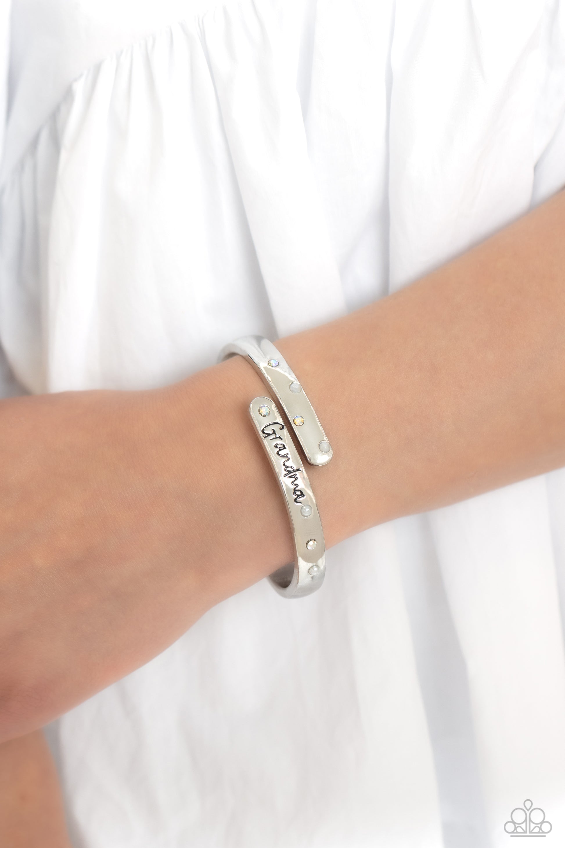 Paparazzi Accessories Gorgeous Grandma - White High-sheen silver curves into a hinged closure around the wrist. Featured on the upper curve, dainty pearls and iridescent rhinestones alternate in a zig-zag pattern for a refined shimmer. The lower curve of