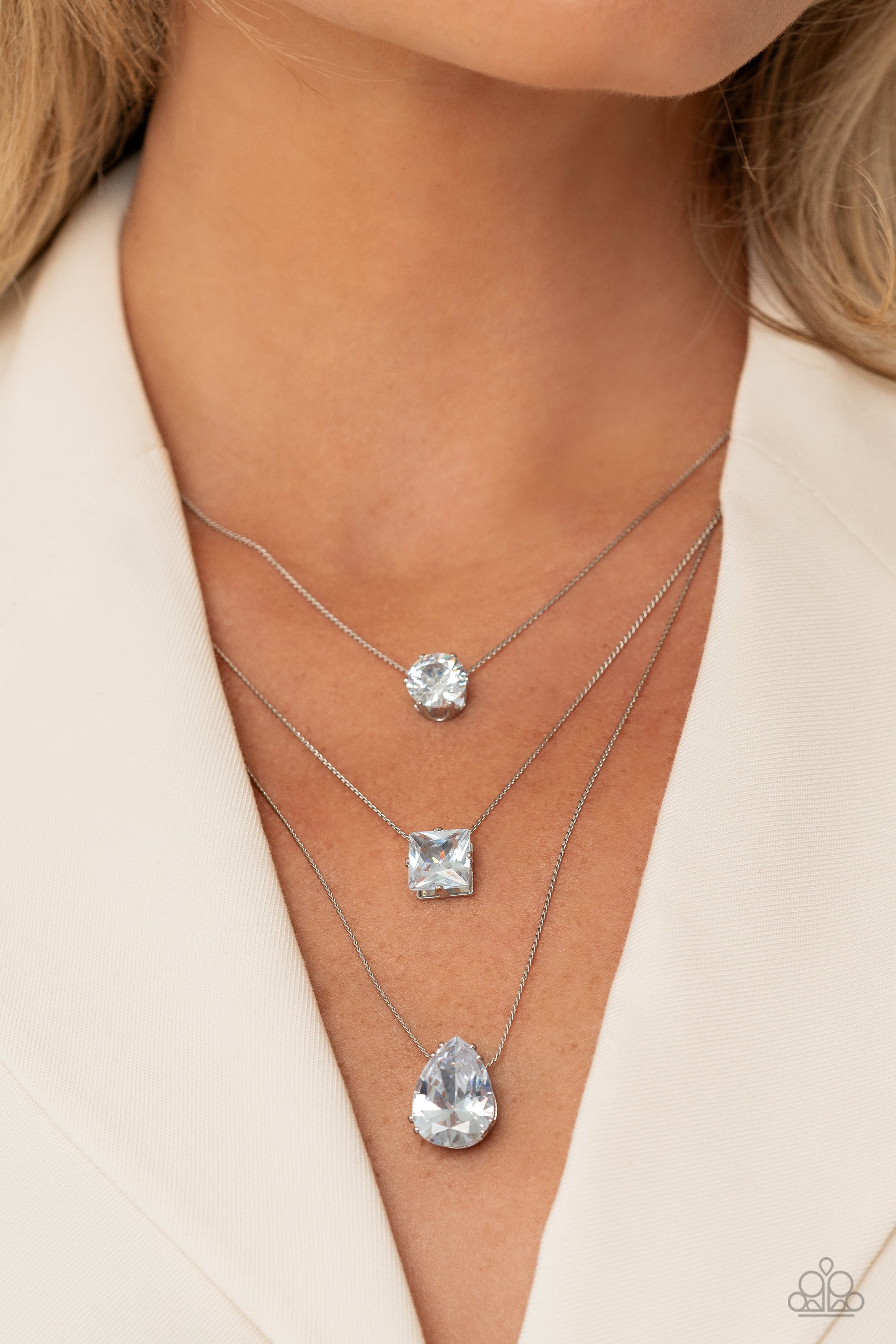 Paparazzi Accessories Lustrous Layers - White Featuring a subtle iridescent finish, exaggerated, faceted round, square, and teardrop gems layer down the chest from three sleek silver dainty chains, in a refined fashion. Features an adjustable clasp closur