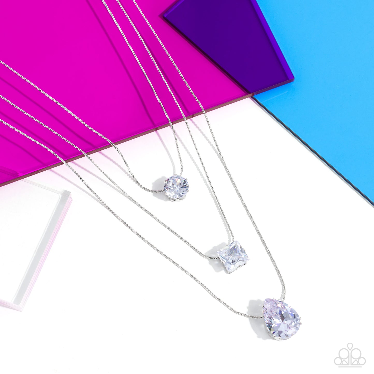 Paparazzi Accessories Lustrous Layers - White Featuring a subtle iridescent finish, exaggerated, faceted round, square, and teardrop gems layer down the chest from three sleek silver dainty chains, in a refined fashion. Features an adjustable clasp closur