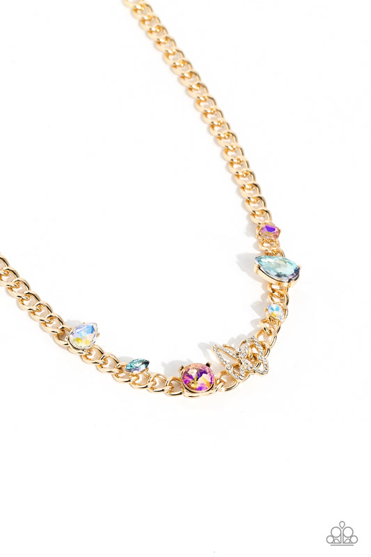 Paparazzi Accessories Storybook Succession - Gold A succession of various gleaming, multicolored gems encased in gold fittings are affixed to a high-sheen, thick gold curb chain, adding dramatic dimension and color to an industrial statement. An airy gold