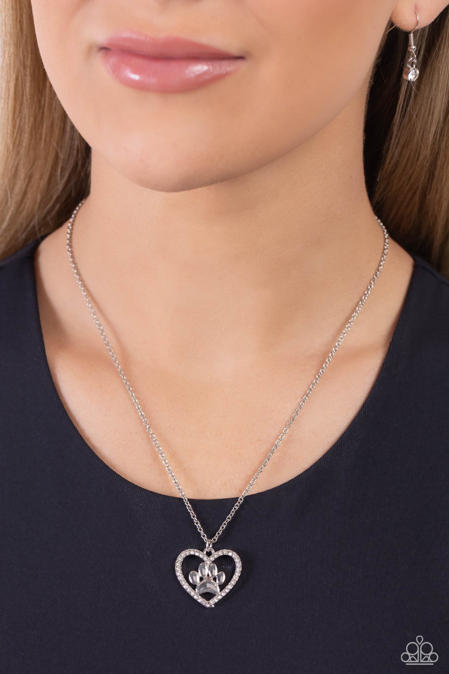 Paparazzi Accessories PET in Motion - White Featuring a paw print charm, an airy rhinestone-embossed heart frame glides down the neckline on a dainty, classic silver chain for a pet-lover inspired pendant. Features an adjustable clasp closure. Sold as one