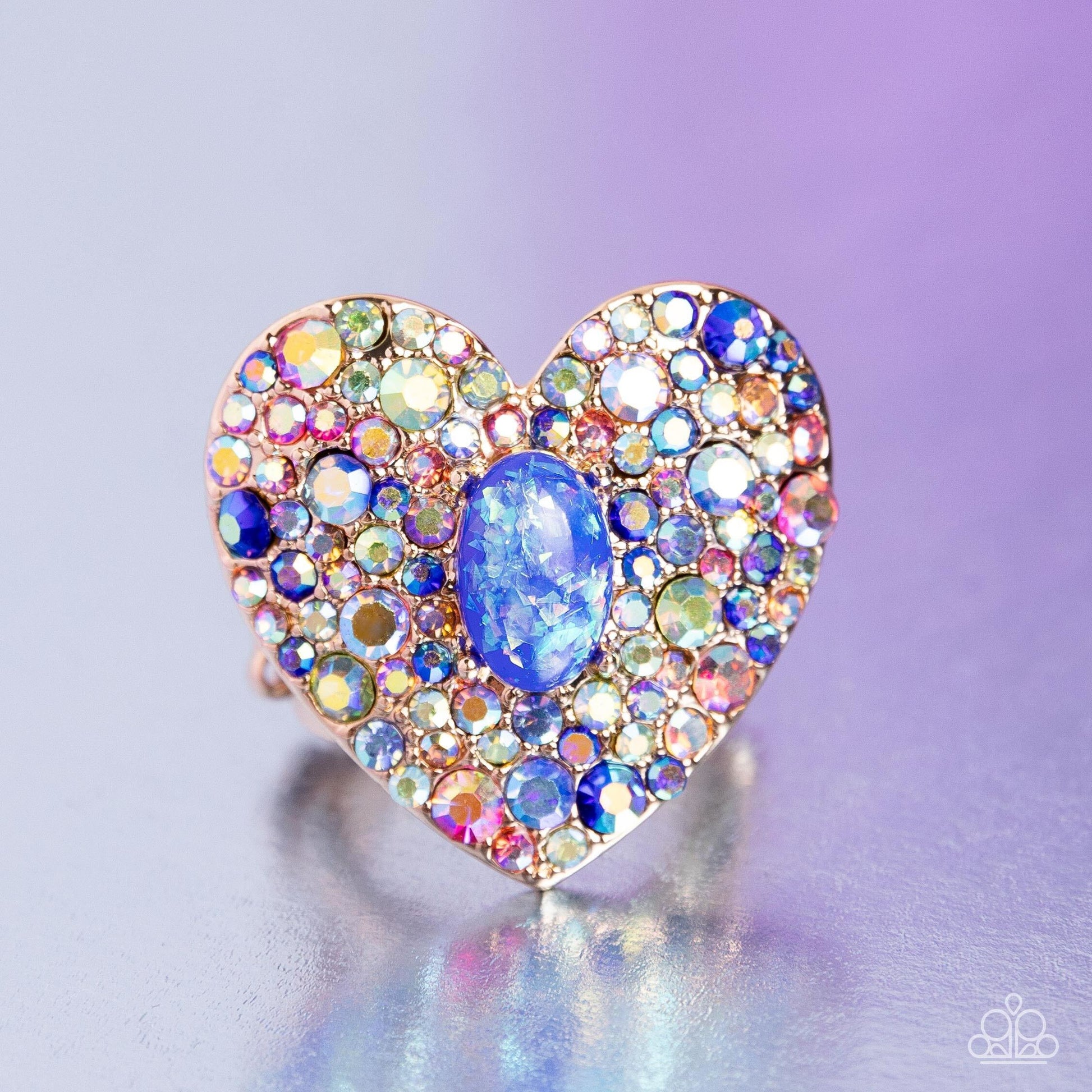 Paparazzi Accessories Bejeweled Beau - Blue Encrusted in brilliant multicolored and iridescent rhinestones, a glittery gold heart frame adorns the center of an airy gold band for a flirtatious finish. Featuring iridescent flecks, an opalescent blue oval b
