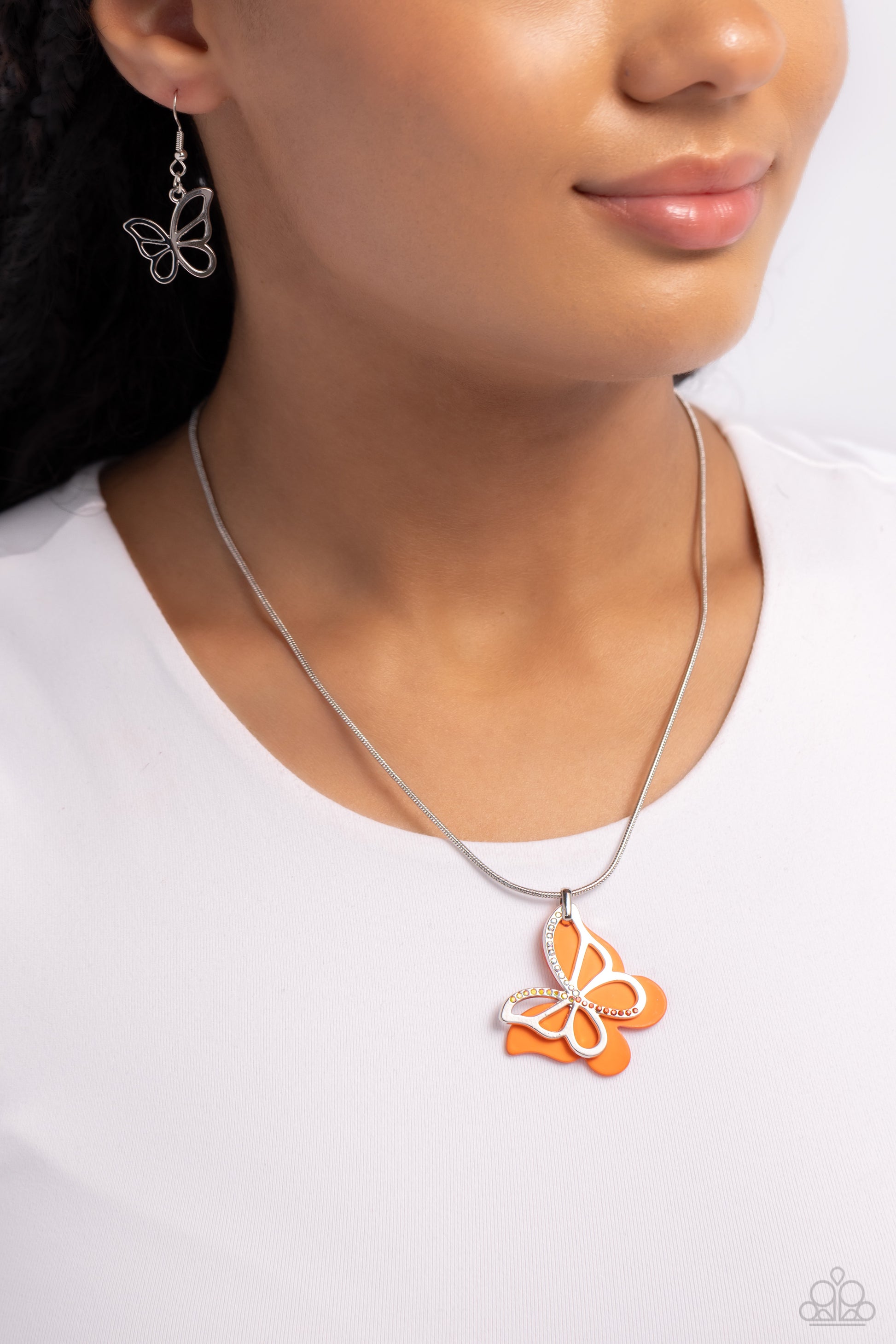 Paparazzi Accessories Detailed Dance - Orange Layered beside a silver butterfly silhouette dotted with light peach, orange, and peachy-iridescent rhinestones, an orange-painted acrylic butterfly flutters from a silver snake chain below the collar for a wh