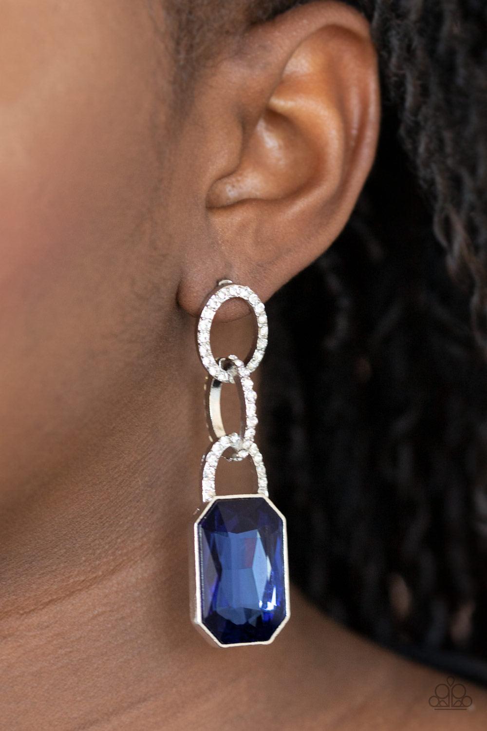 Paparazzi Accessories Superstar Status - Blue An oversized blue emerald-cut rhinestone swings from the bottom of white rhinestone encrusted links, creating a gorgeously dramatic lure. Earring attaches to a standard post fitting. Sold as one pair of post e