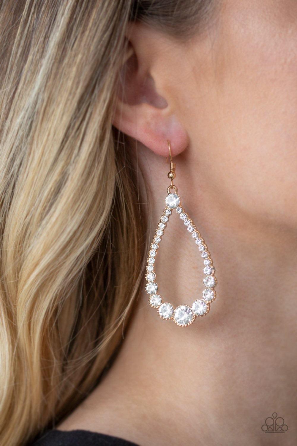 Paparazzi Accessories Token Twinkle - Gold A collection of glassy white rhinestones are encrusted along the front of an ornate gold teardrop. The sparkling rhinestones gradually increase in size at the bottom of the lure for a sophisticated finish. Earrin
