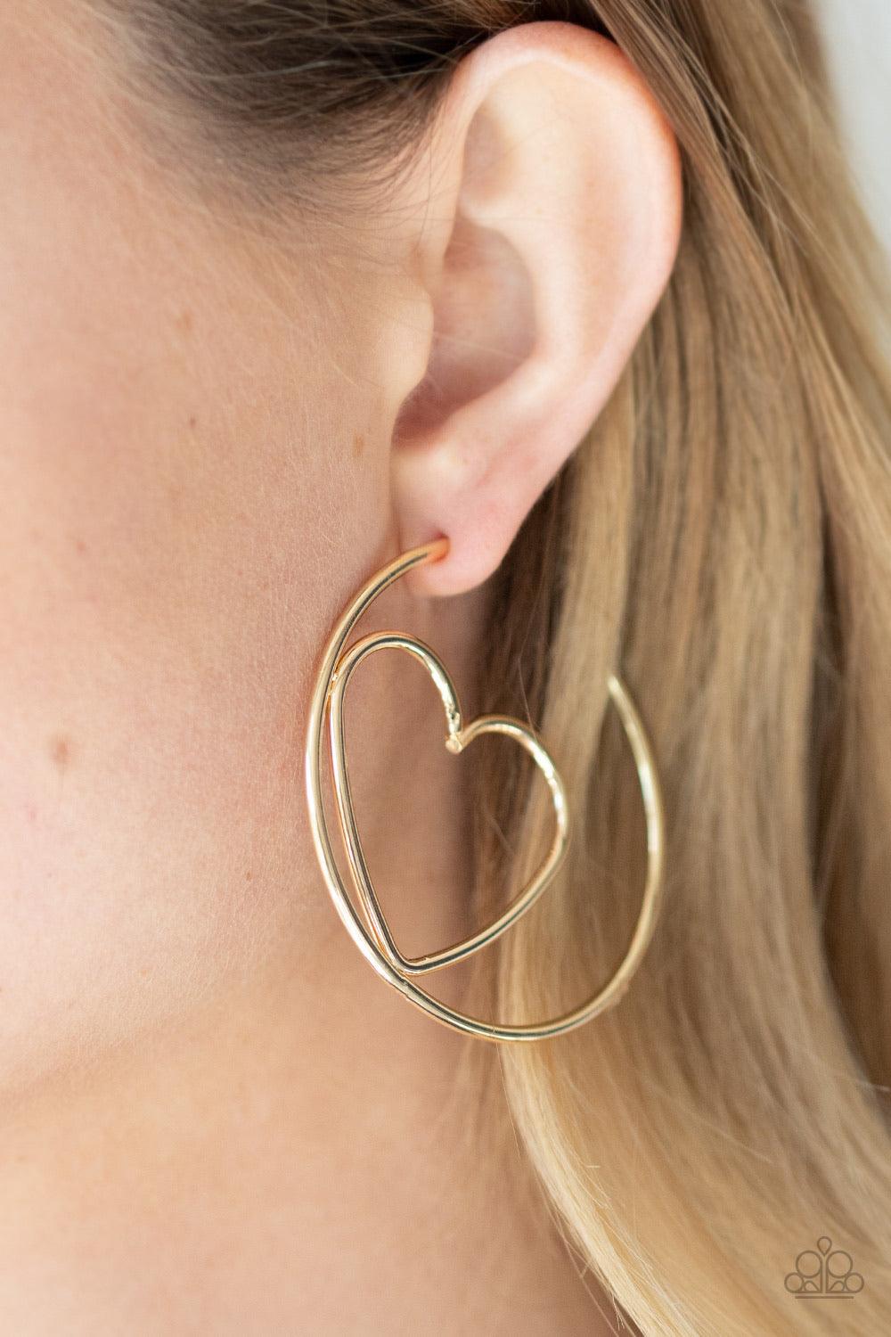 Paparazzi Accessories Love At First BRIGHT - Gold Glistening gold wire delicately bends into an airy heart frame inside a classic gold hoop, creating a flirtatious display. Earring attaches to a standard post fitting. Hoop measures approximately 2" in dia