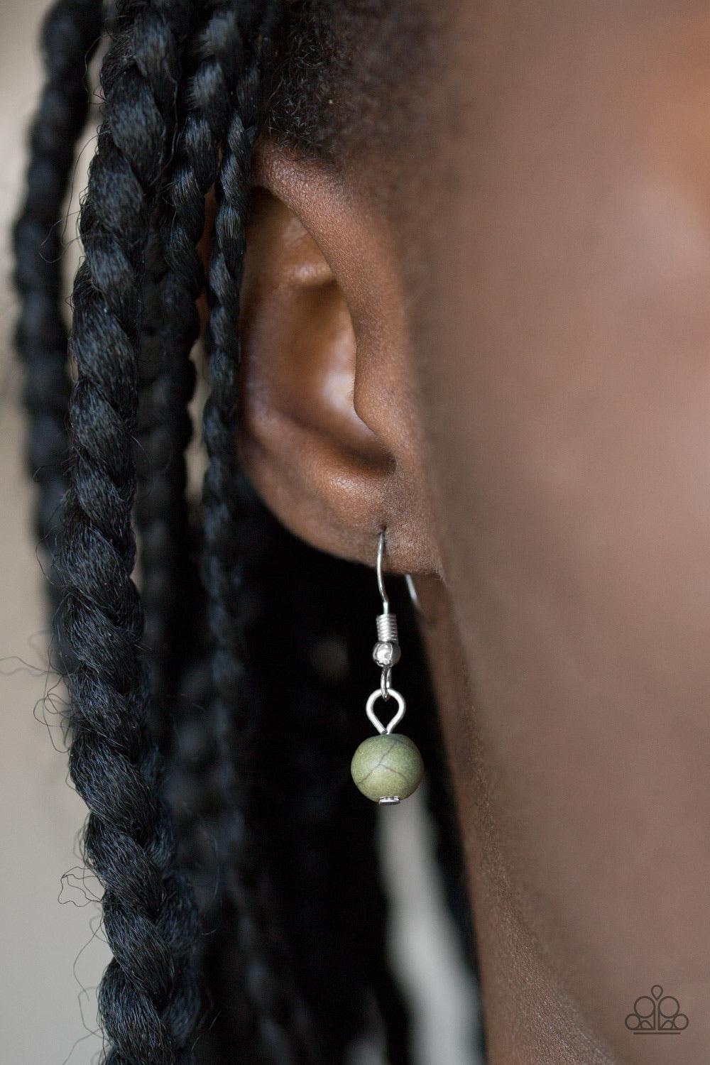 Paparazzi Accessories Bon Voyager - Green An earthy green stone is pressed into the center of a shimmery silver disc radiating with glistening tribal details. Swinging from the bottom of a lengthened silver chain, the bold pendant gives way to a fringe of