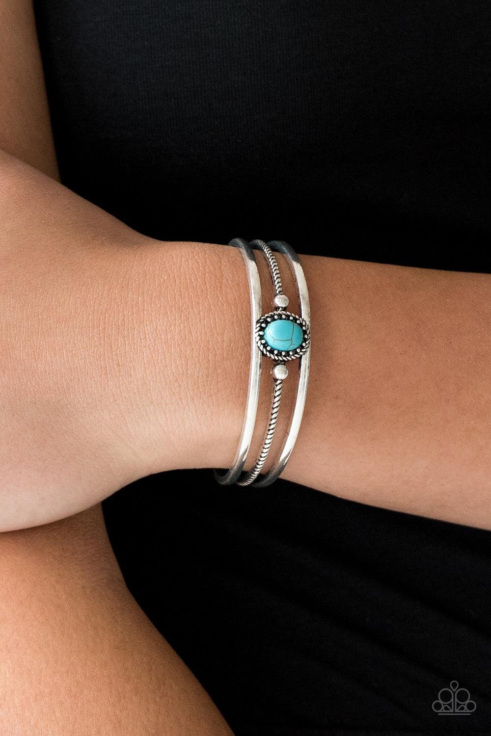 Paparazzi Accessories Borderline Borderland - Blue Serrated and smooth silver bars arc across the wrist, coalescing into an airy cuff. Infused with a studded frame, a refreshing turquoise stone is pressed into the center of the cuff for a seasonal look. S