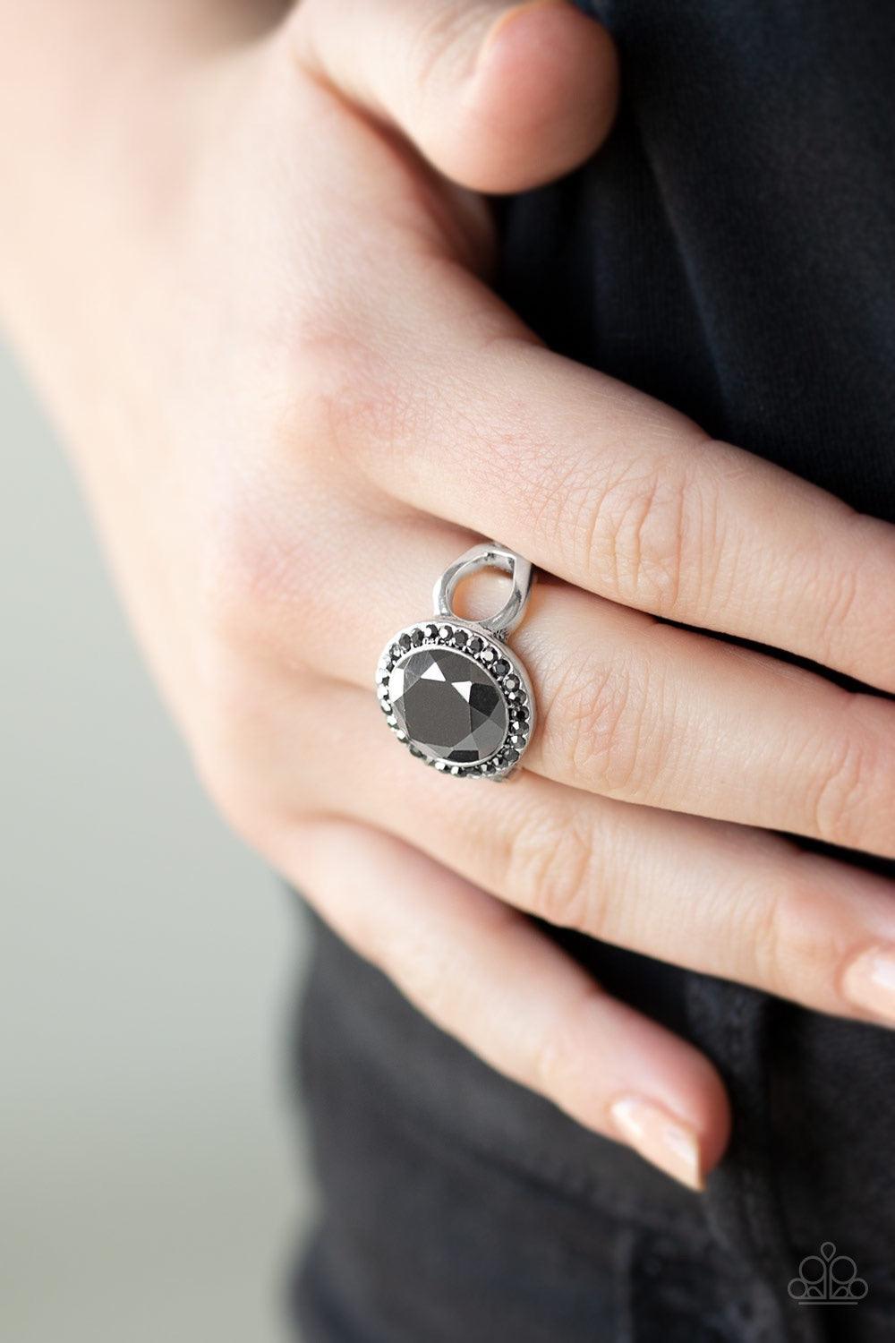 Paparazzi Accessories It’s Gonna GLOW! - Black An oversized hematite gem is pressed into the center of a round silver frame encrusted in a ring of radiant hematite rhinestones for a regal flair. Features a dainty stretchy band for a flexible fit. Jewelry
