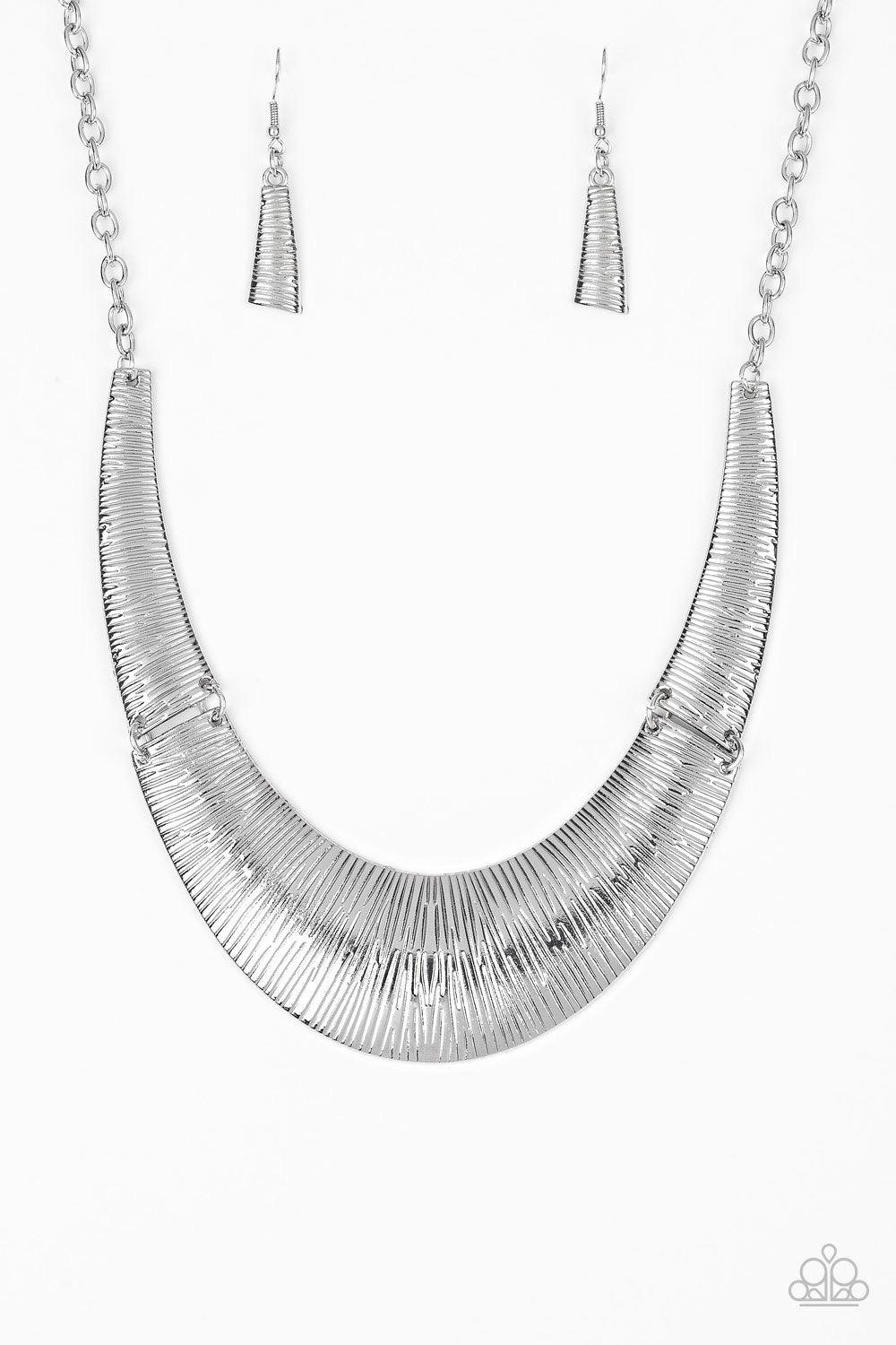 Paparazzi Accessories Feast or Famine - Silver Etched in linear patterns, dramatic silver plates connect below the collar, joining into a fierce crescent-shaped pendant for a statement making look. Features an adjustable clasp closure. Sold as one individ
