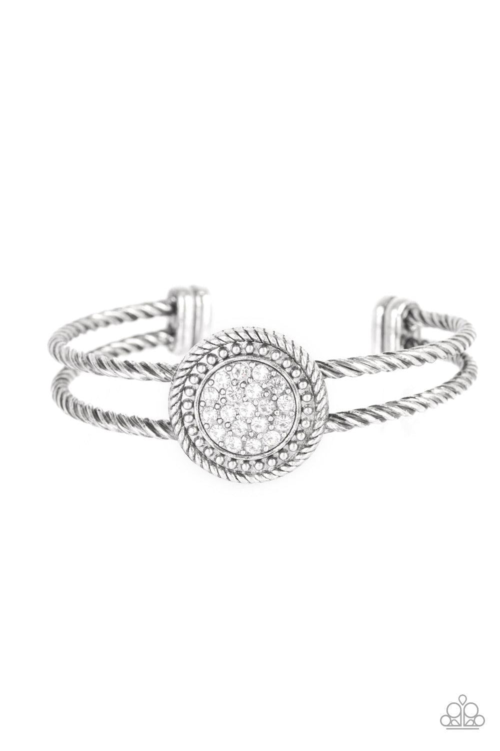 Paparazzi Accessories Definitely Dazzling - White Brushed in an antiqued shimmer, twisted silver bars arc across the finger, coalescing into an airy cuff. Radiating in silver studs and glittery white rhinestones, a round silver frame adorns the center for