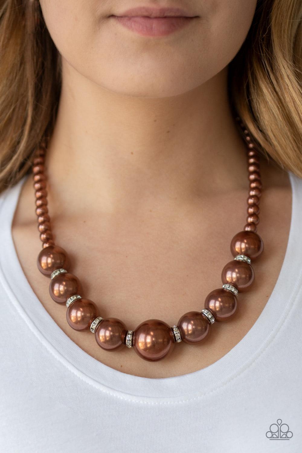 Paparazzi Accessories SoHo Socialite - Brown Threaded along an invisible wire, classic brown pearls give way to an alternating collection of oversized brown pearls and white rhinestone encrusted rings below the collar for a timeless sparkle. Features an a