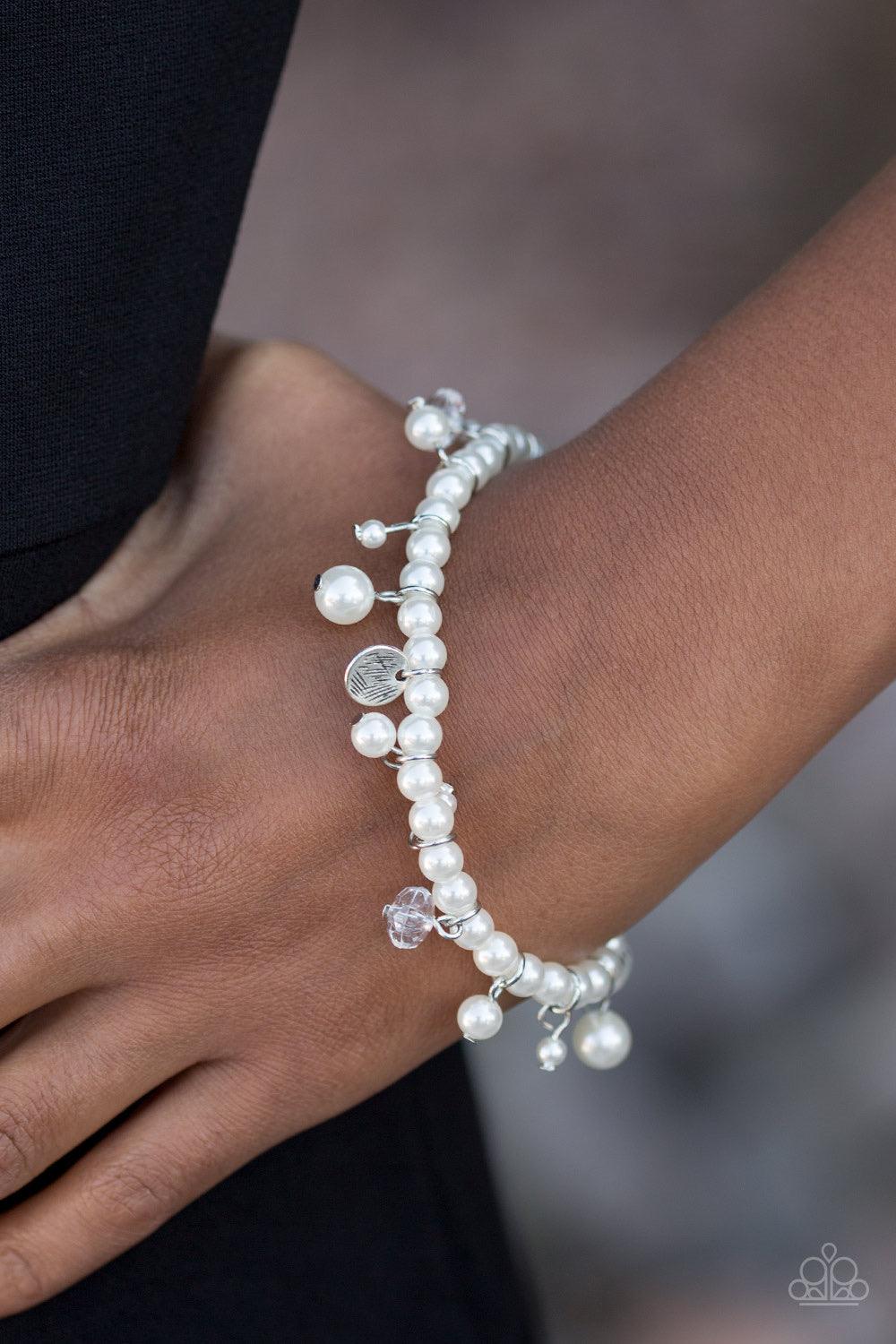 Paparazzi Accessories Treasure Chest Chic - White Classic white pearls are threaded along an elastic stretchy band. Etched in glistening textures, shimmery silver discs, pearl accents, and glittery crystal-like beading swing from the wrist, adding a refin