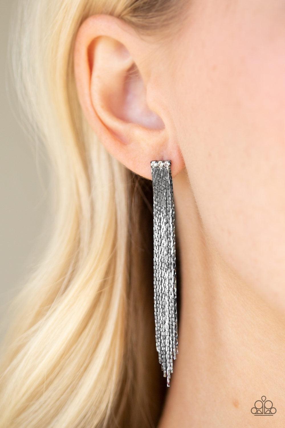 Paparazzi Accessories Night At The Oscar - Black A tassel of flat gunmetal chain cascades from a row of three white rhinestones. Brushed in a high sheen reflective finish, the streaming chains coalesce into a brilliant shimmer. Earring attaches to a stand
