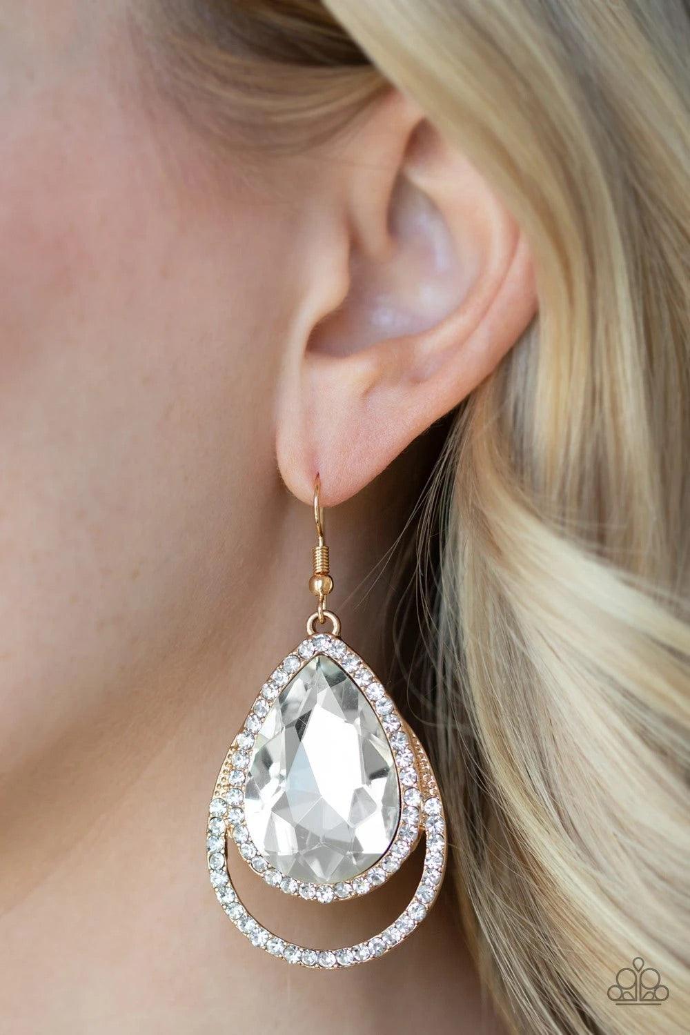 Paparazzi Accessories Famous - Gold A dramatically oversized white teardrop gem is pressed into a doubled gold frame encrusted in countless white rhinestones for a blinding look. Earring attaches to a standard fishhook fitting. Sold as one pair of earring