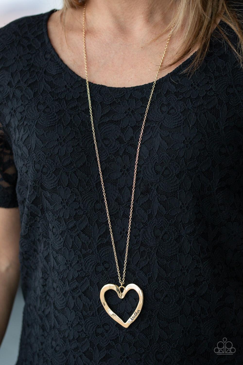 Paparazzi Accessories A Mother’s Love - Gold Swinging from the bottom of a lengthened gold chain, an asymmetrical heart pendant is stamped in the word, "mom" and dotted with a single white rhinestone for a whimsical look. Features an adjustable clasp clos