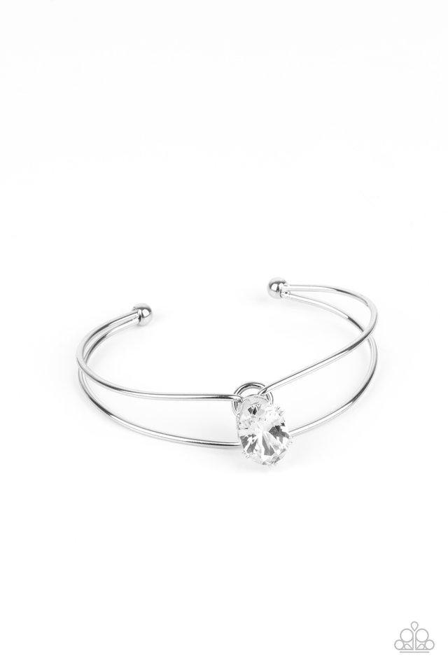 Paparazzi Accessories GLOW No Mercy - White A dramatically oversized white rhinestone is fitted in place atop the center of a silver wire cuff, creating a jaw-dropping display around the wrist. Sold as one individual bracelet. Jewelry