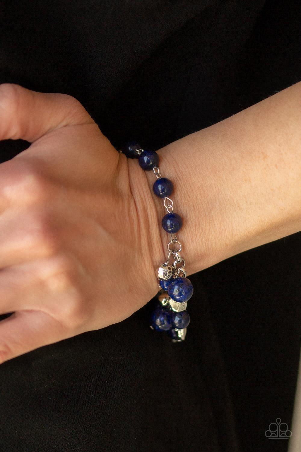 Paparazzi Accessories Glossy Glow - Blue An array of mismatched silver charms and beads swings from a glassy blue beaded bracelet around the wrist, creating a whimsical fringe. Features an adjustable clasp closure. Jewelry
