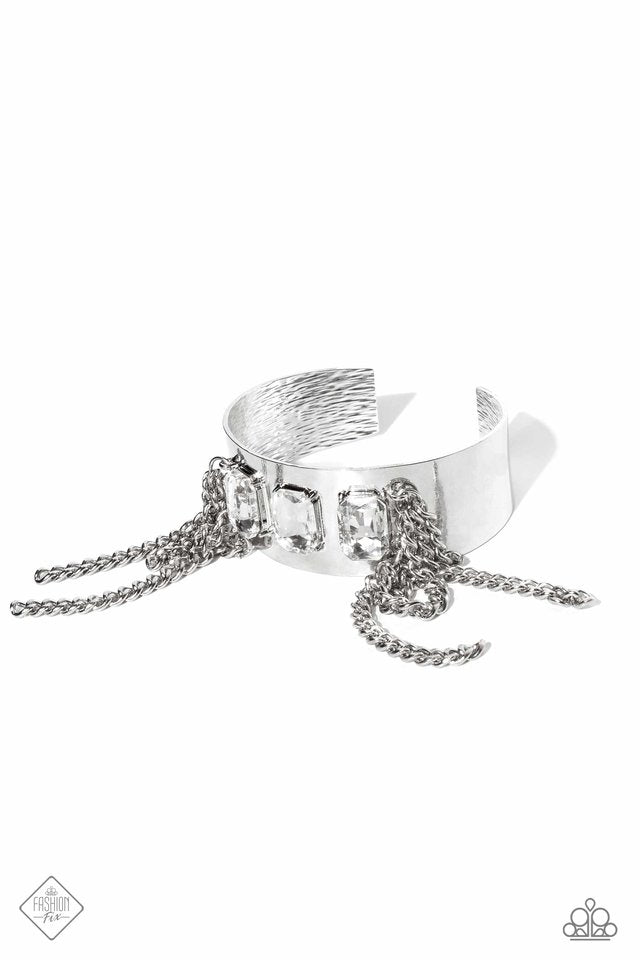 Paparazzi Accessories CHAIN Showers - White A thick, industrial silver cuff is topped by three brilliant white, emerald-cut gems. Strands of silver curb chain stream from each side of the trio of glitz, adding undeniable drama and eye-catching movement to