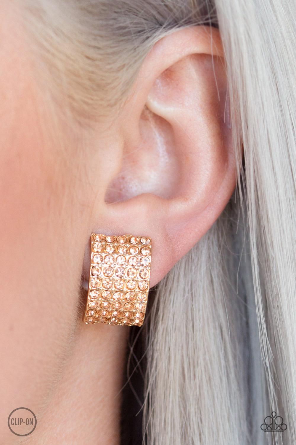 Paparazzi Accessories Hollywood HotShot - Gold *Clip-On Encrusted in row after row of glittery peach rhinestones, a radiant gold ribbon curls around the ear for a glamorous look. Earring attaches to a standard clip-on fitting. Sold as one pair of clip-on