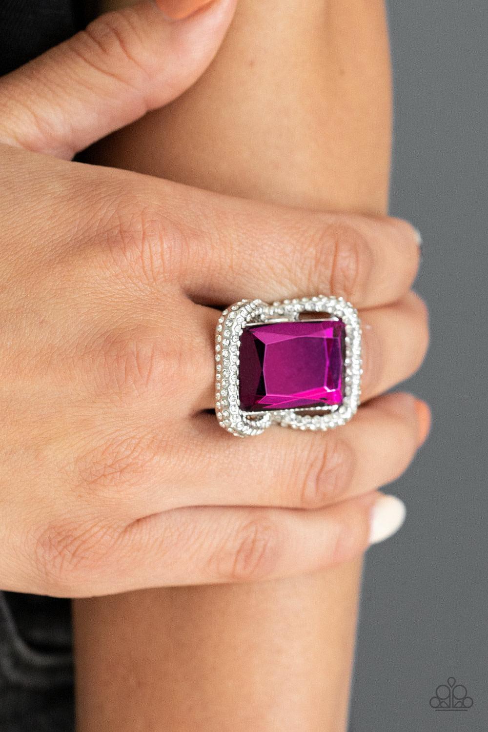 Paparazzi Accessories Deluxe Decadence - Pink Featuring a regal emerald style cut, an oversized pink gem nestles inside a rounded square silver frame encrusted in glassy white rhinestones for a dramatically glamorous look. Features a stretchy band for a f