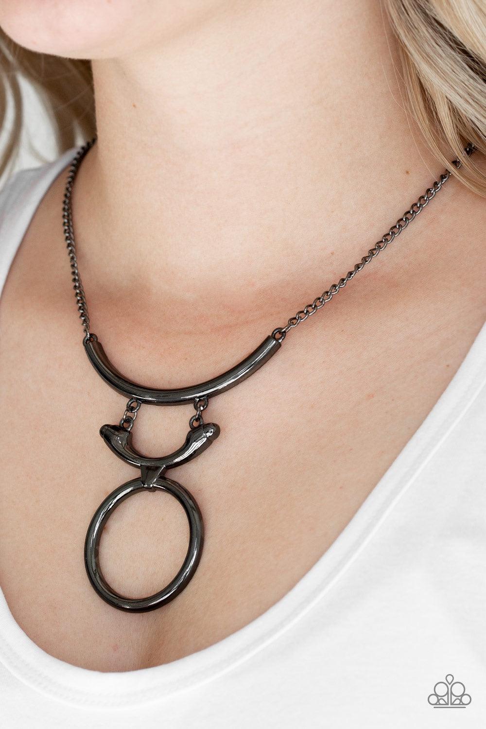Paparazzi Accessories Walk Like An Egyptian - Black Two glistening gunmetal crescents attach to a large gunmetal hoop, creating a tribal inspired pendant below the collar. Features an adjustable clasp closure. Jewelry