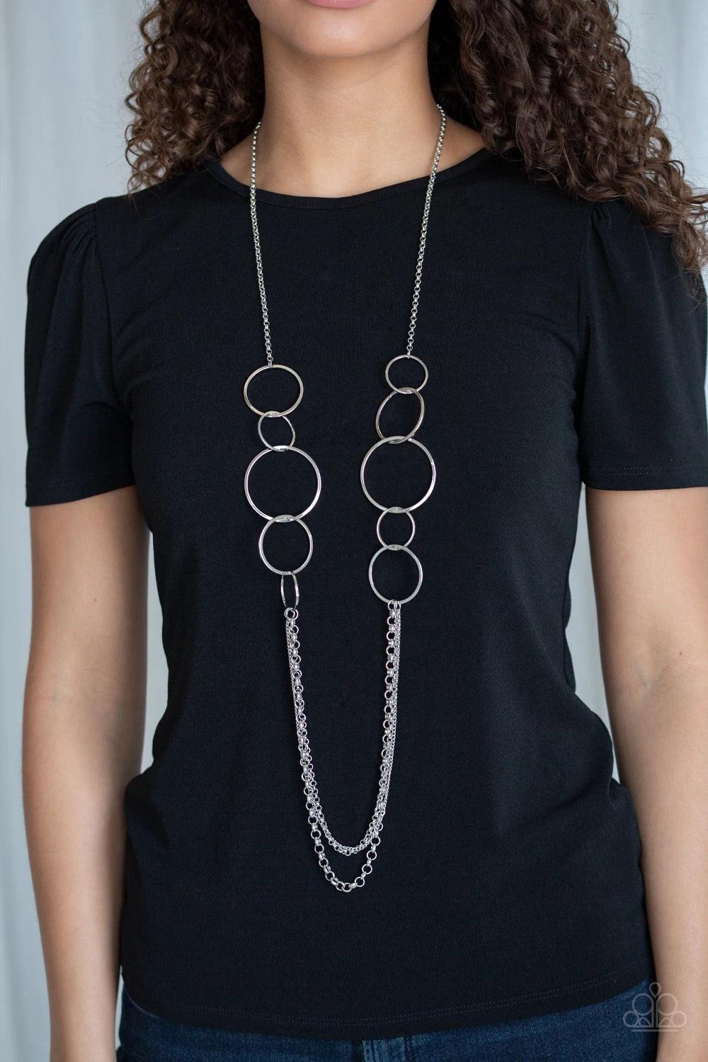 Paparazzi Accessories Ring In The Radiance - Silver A collection of interlocking silver rings give way to layers of mismatched silver chains down the chest, creating a stunning tone-on-tone statement piece. Features an adjustable clasp closure. Sold as on