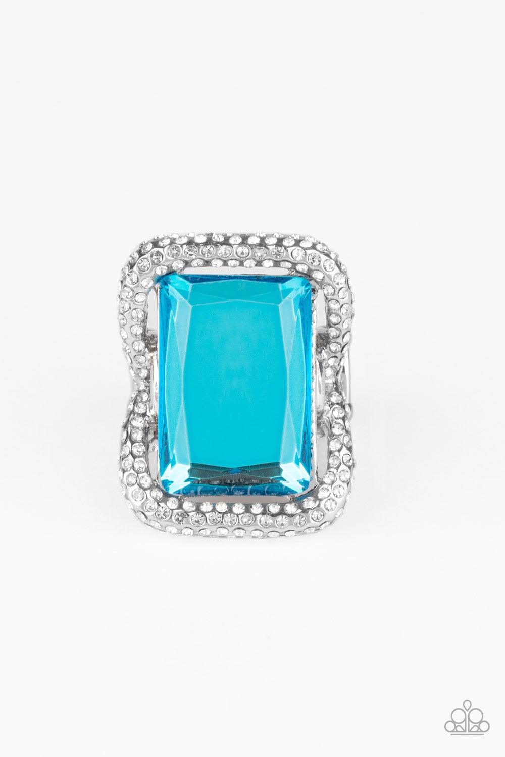 Paparazzi Accessories Deluxe Decadence - Blue Featuring a regal emerald style cut, an oversized blue gem nestles inside a rounded square silver frame encrusted in glassy white rhinestones for a dramatically glamorous look. Features a stretchy band for a f