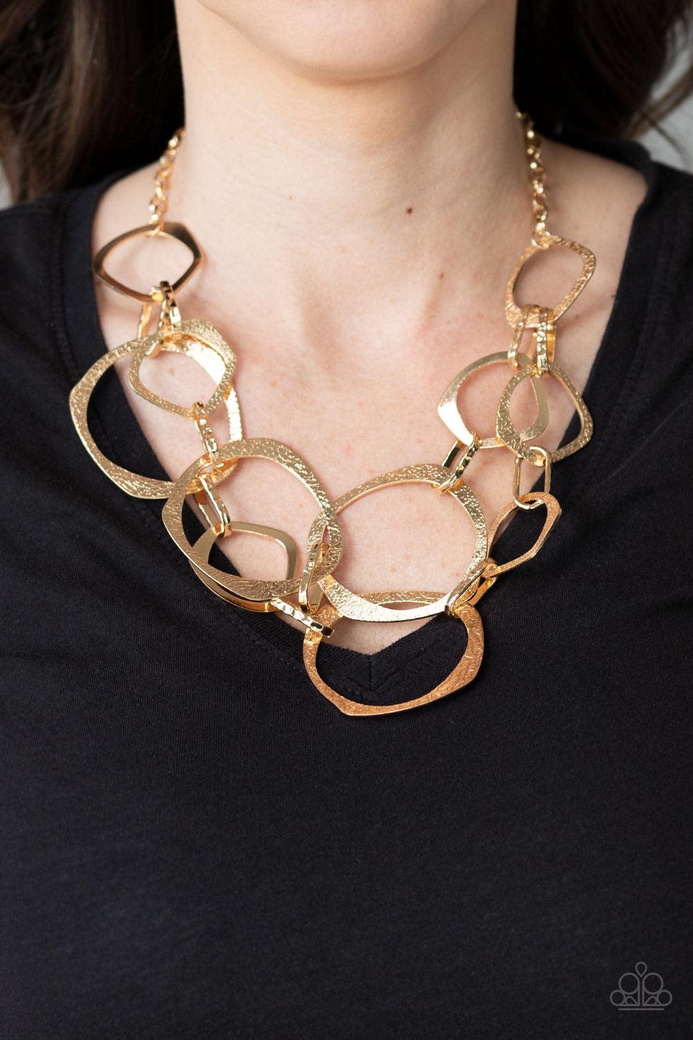 Paparazzi Accessories Salvage Yard - Gold Hammered in shimmery detail, oversized asymmetrical gold rings and gritty gold links boldly link below the collar in two dramatic rows for a sassy industrial look. Features an adjustable clasp closure. Sold as one