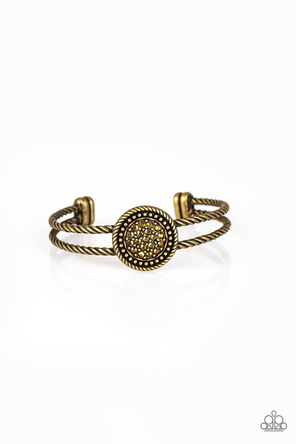 Paparazzi Accessories Definitely Dazzling - Brass Brushed in an antiqued shimmer, twisted brass bars arc across the finger, coalescing into an airy cuff. Radiating in brass studs and glittery aurum rhinestones, a round brass frame adorns the center for an