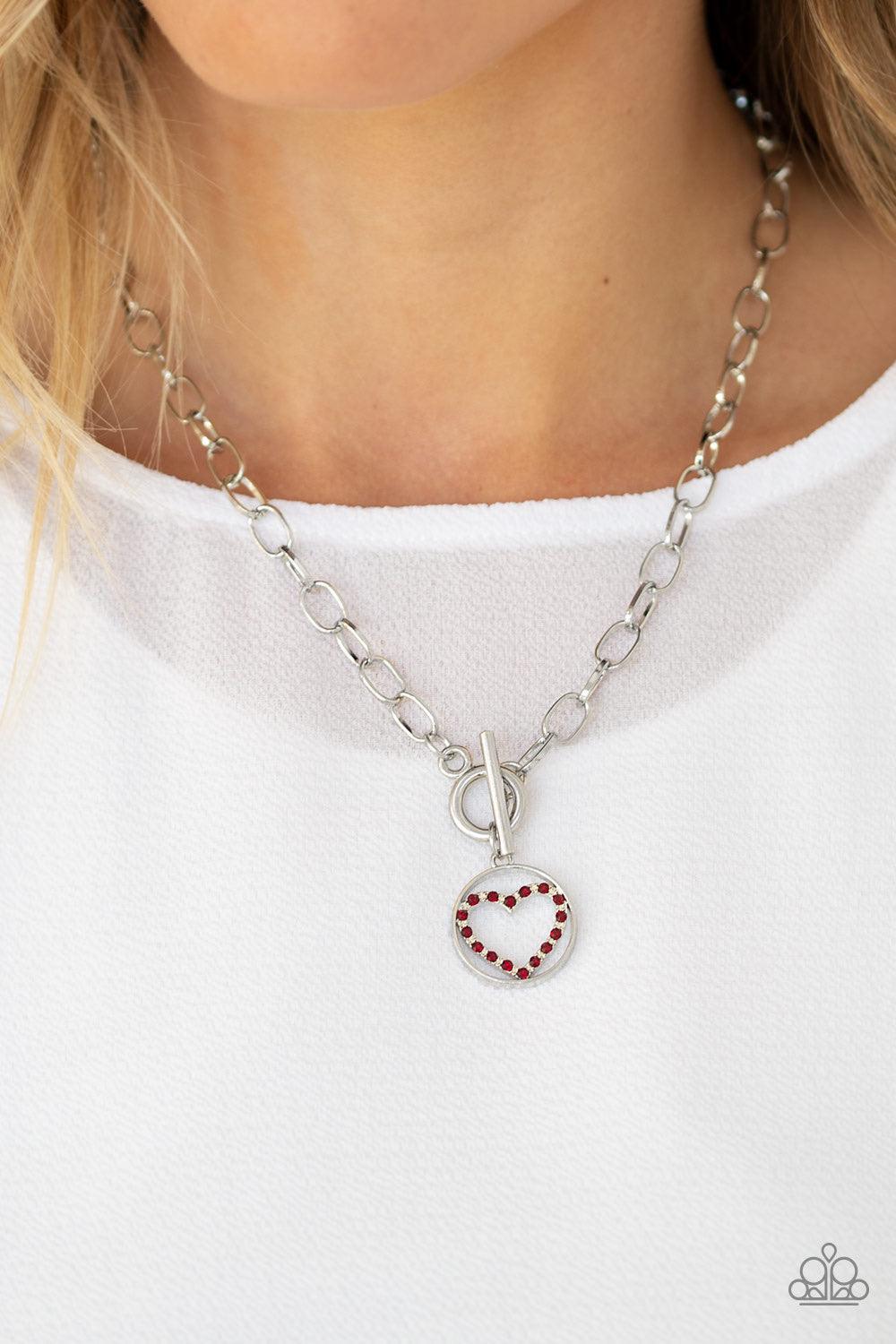 Paparazzi Accessories With My Whole Heart ~Red A red rhinestone encrusted silver heart is nestled inside a shiny silver hoop, creating a charming pendant at the bottom of an exaggerated silver chain. Features a toggle closure.