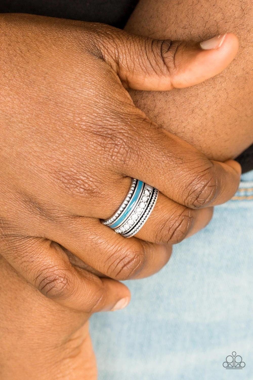Paparazzi Accessories Rich Rogue - Blue A shiny blue strip of color runs along the bottom of a row of glassy white rhinestones. Infused with silver textures, the mismatched details coalesce into one thick band across the finger. Features a stretchy band f