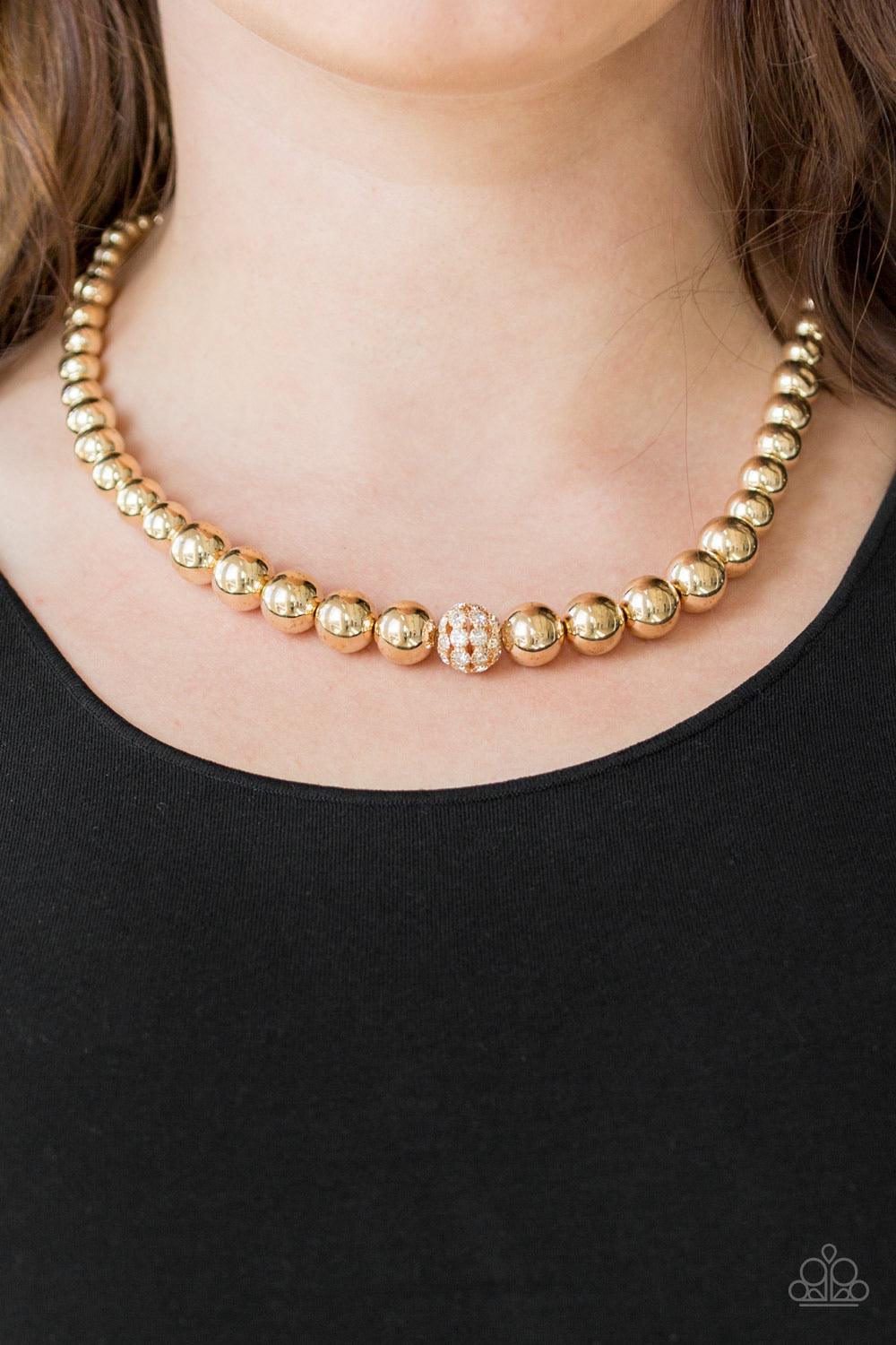 Paparazzi Accessories High-Stakes FAME - Gold Gradually increasing in size near the center, glistening gold beads are threaded along an invisible wire below the collar. Encrusted in glassy white rhinestones, a sparkling gold bead adorns the center for a r