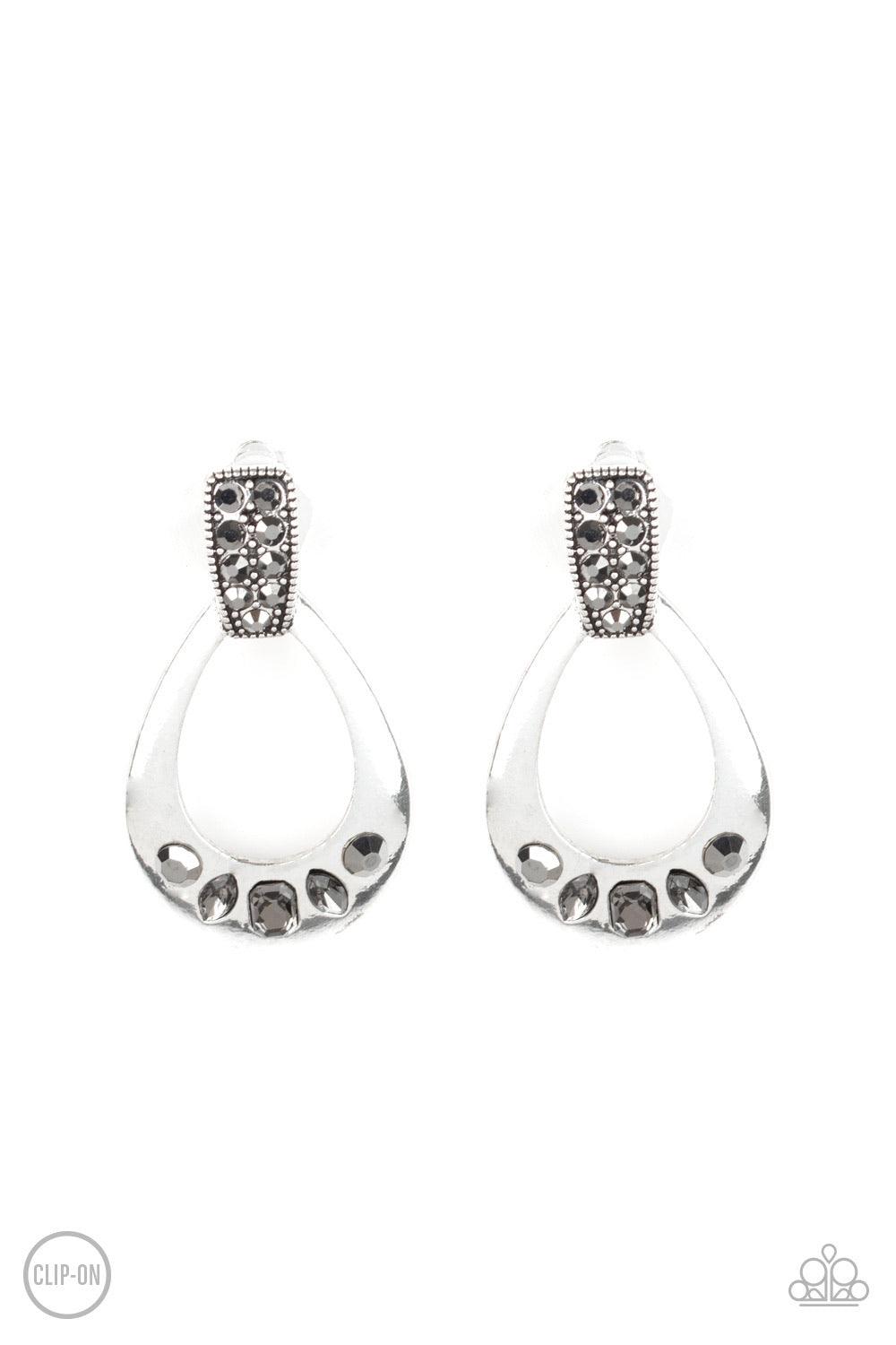 Paparazzi Accessories Broker Babe - Silver *Clip-On The bottom of a shimmery silver teardrop frame is encrusted in a mismatched collection of smoky and hematite rhinestones as it swings from the bottom of a hematite rhinestone encrusted fitting for a refi