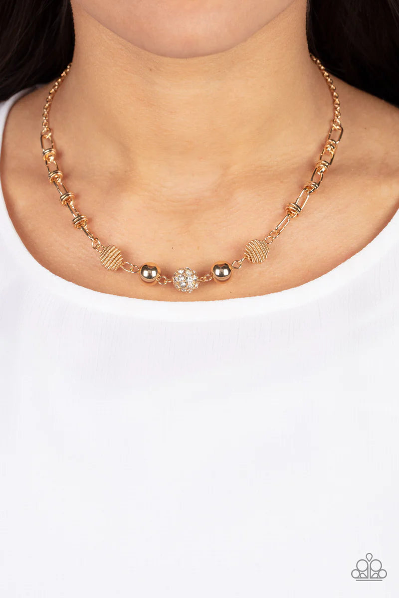 Paparazzi Accessories Taunting Twinkle - Gold Pairs of gold coiled and smooth gold beads flank a white rhinestone encrusted bead along an oval and gold disc linked chain, creating a glitzy combination below the collar. Features an adjustable clasp closure