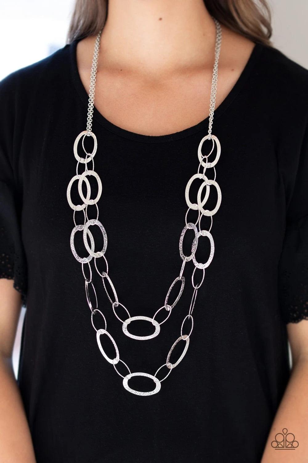 Paparazzi Accessories Glimmer Goals - Silver Delicately hammered in shimmery textures, two rows of glistening silver hoops layer down the chest for a sleek look. Features an adjustable clasp closure. Sold as one individual necklace. Includes one pair of m