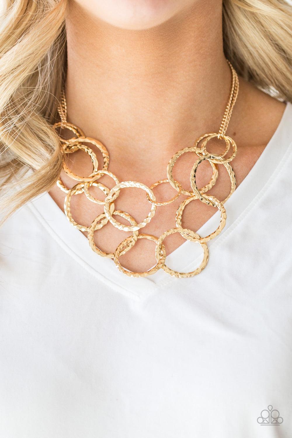 Paparazzi Accessories Radiant Ringmaster - Gold Varying in size, gold rings are delicately hammered with light catching shimmer. The glistening rings link below the collar, draping into two layered rows for an edgy finish. Features an adjustable clasp clo