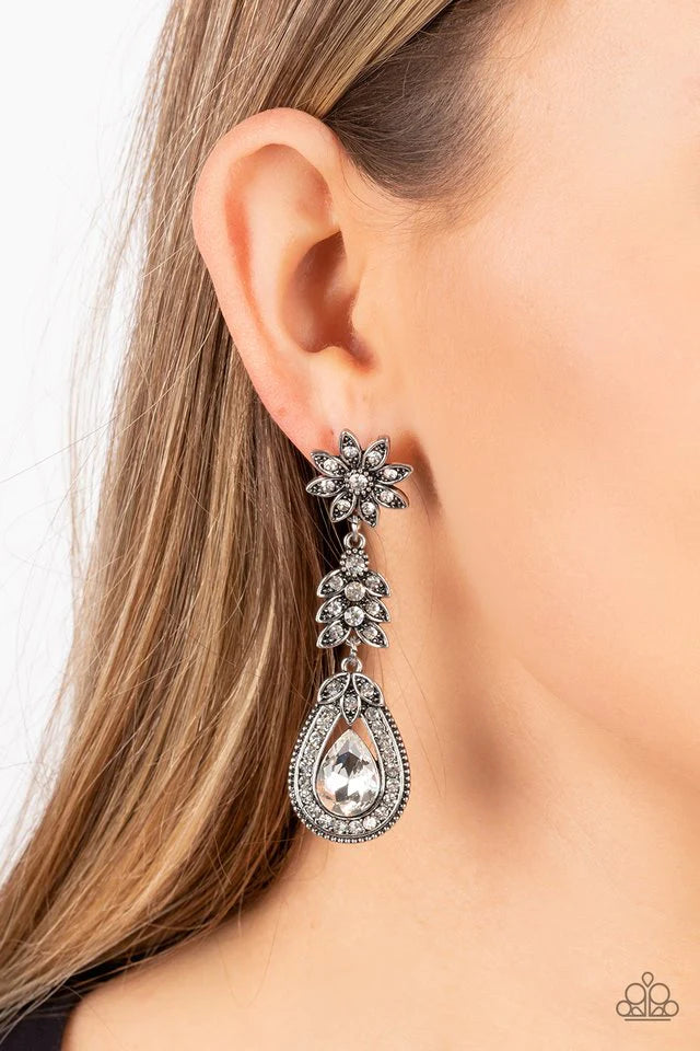 Paparazzi Accessories Floral Fantasy - White Dotted in dainty white rhinestones, a studded silver flower gives way to a leafy frame that is delicately suspended above a decorative white rhinestone dotted teardrop frame. An oversized teardrop gem seemingly