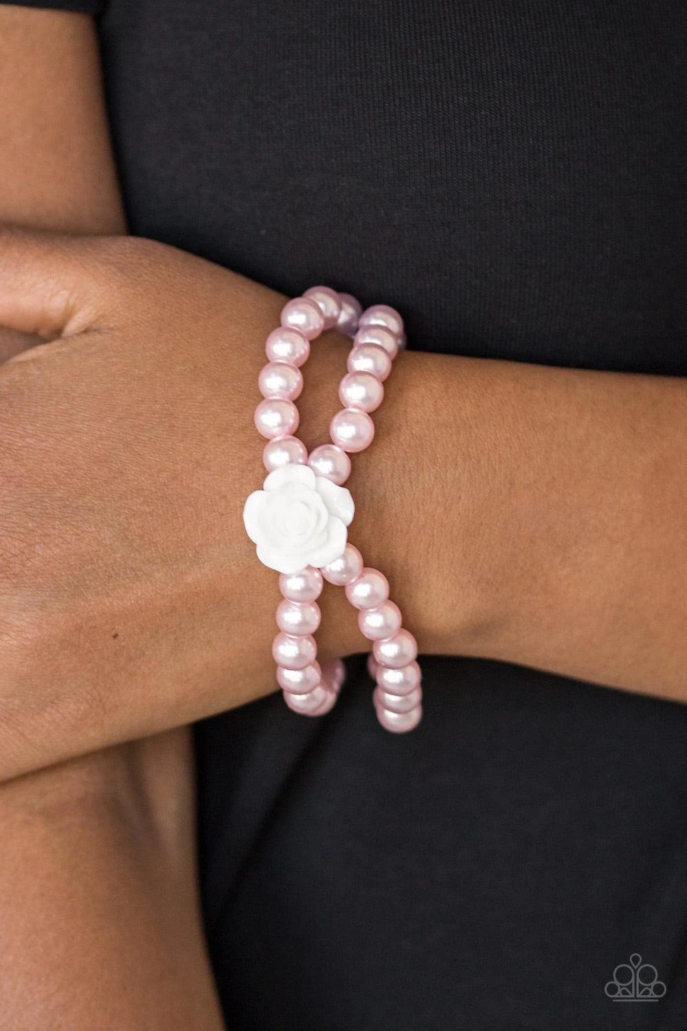 Paparazzi Accessories Posh and Posy - Pink Connected by a flirty white resin rose, classic pink pearls are threaded along stretchy bands around the wrist for a vintage inspired fashion. Sold as one individual bracelet Jewelry